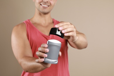 Young man holding deodorant on beige background, closeup. Mockup for design