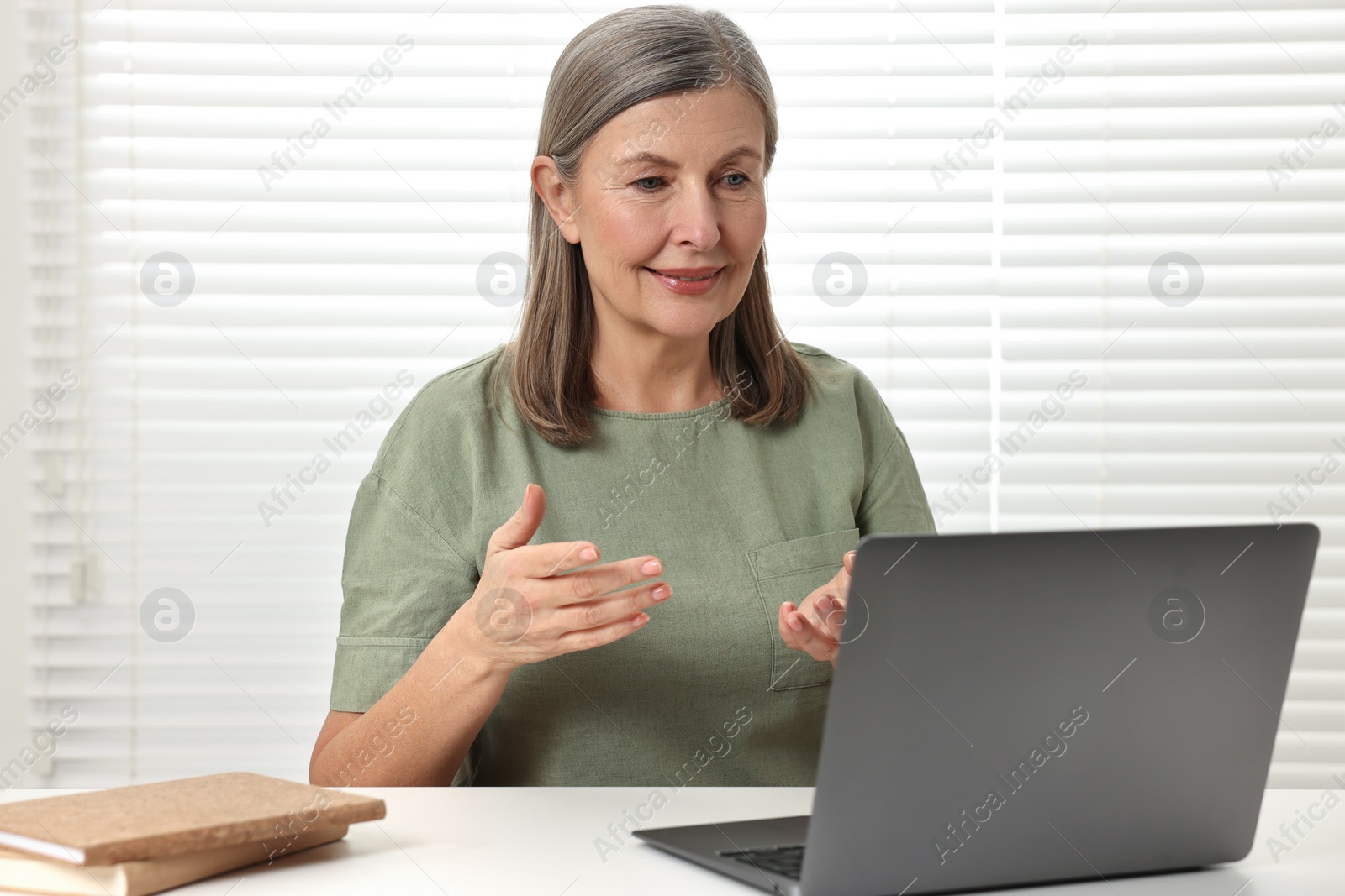 Photo of Happy woman having video chat via laptop at table indoors