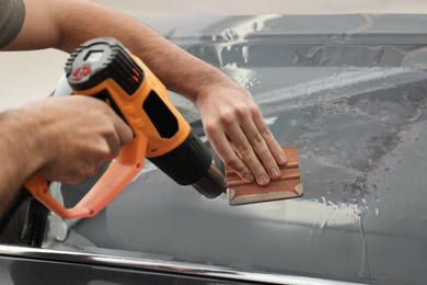 Worker tinting car window with heat gun in workshop, closeup