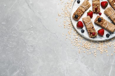 Photo of Tasty granola bars and ingredients on light grey table, top view. Space for text