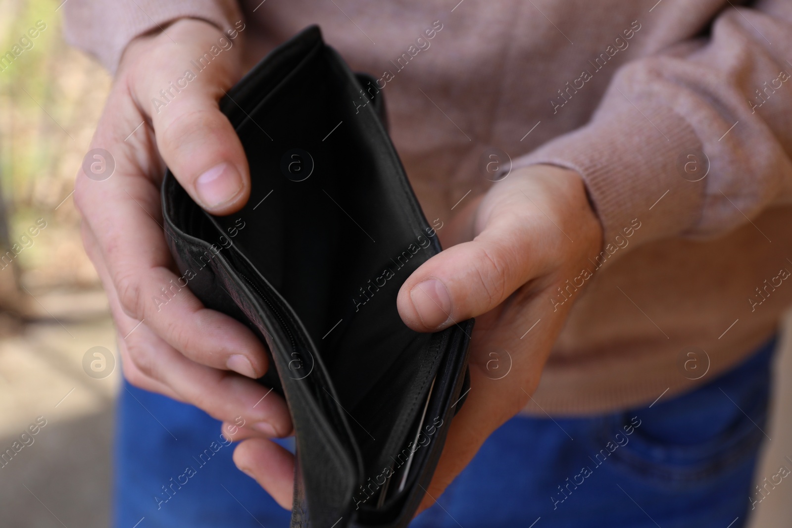 Photo of Poor man holding empty wallet outdoors, closeup