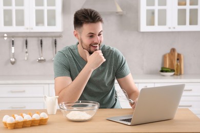 Photo of Happy man learning to cook with online video on laptop at table in kitchen. Time for hobby