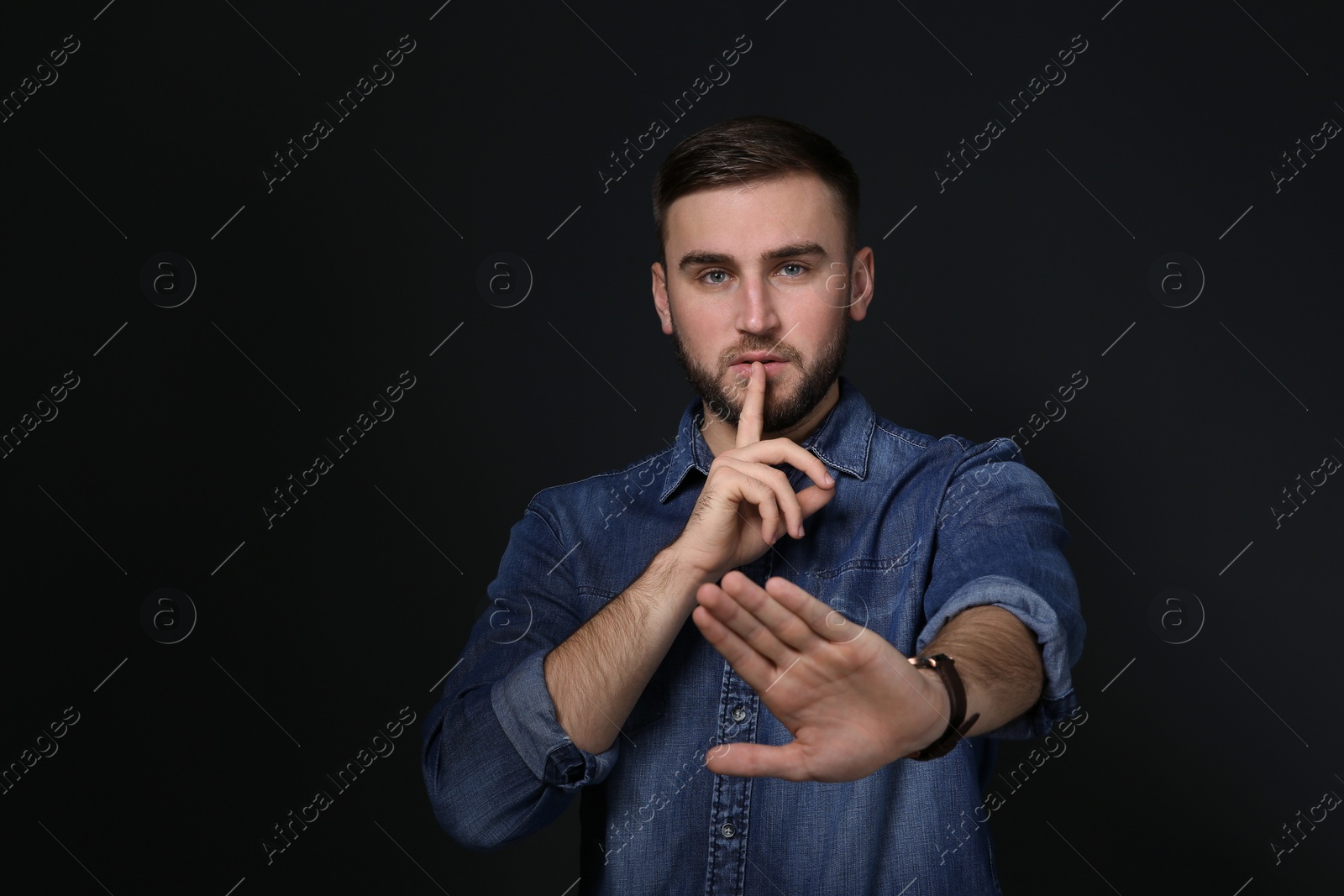 Photo of Man showing HUSH gesture in sign language on black background