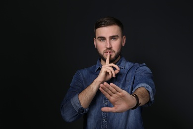 Photo of Man showing HUSH gesture in sign language on black background