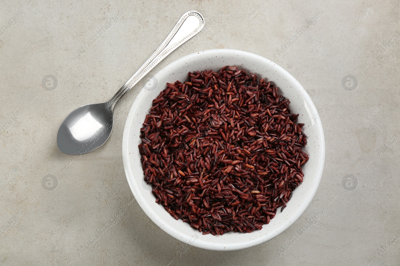 Photo of Tasty brown rice and spoon on light grey table, flat lay