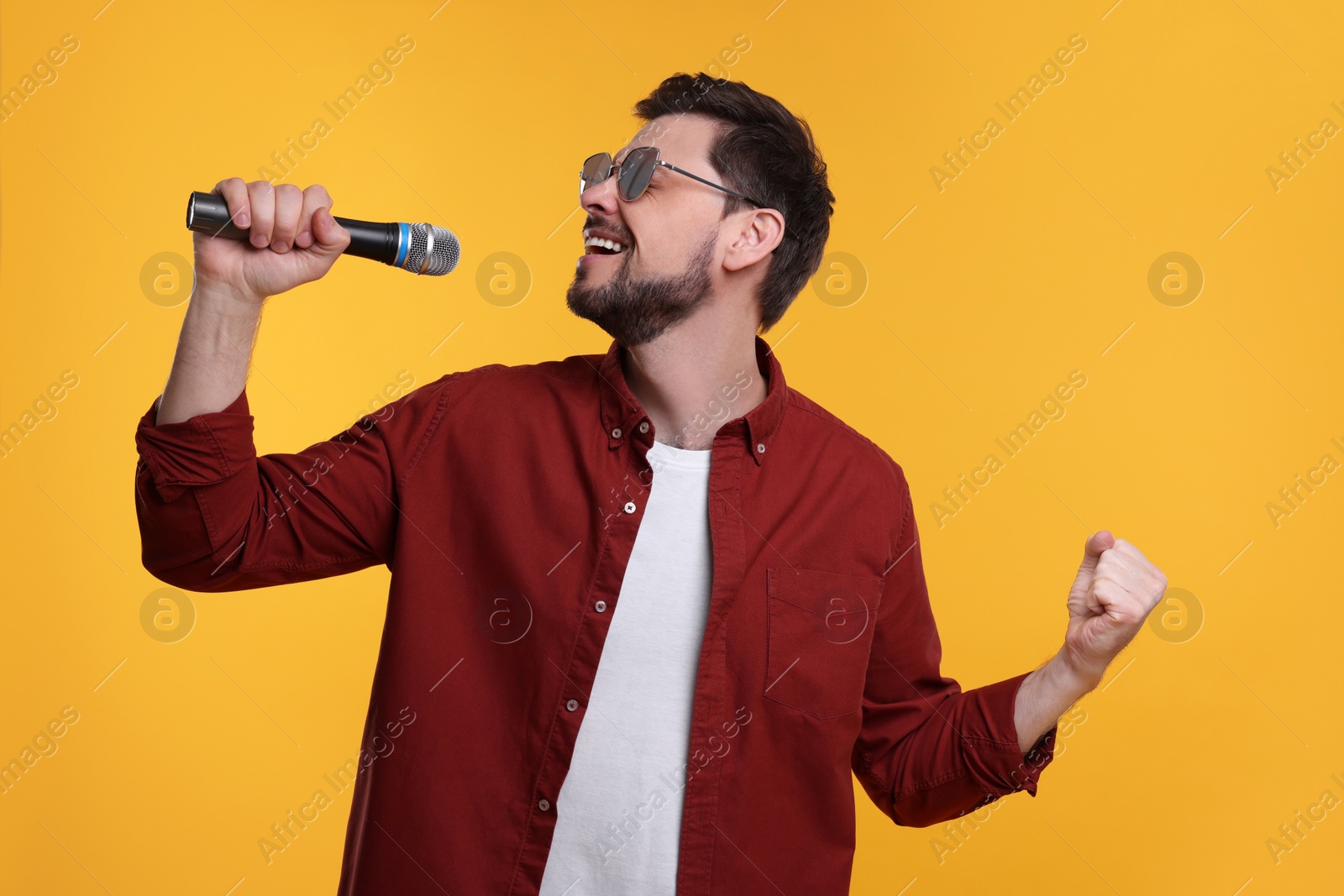 Photo of Handsome man with sunglasses and microphone singing on yellow background