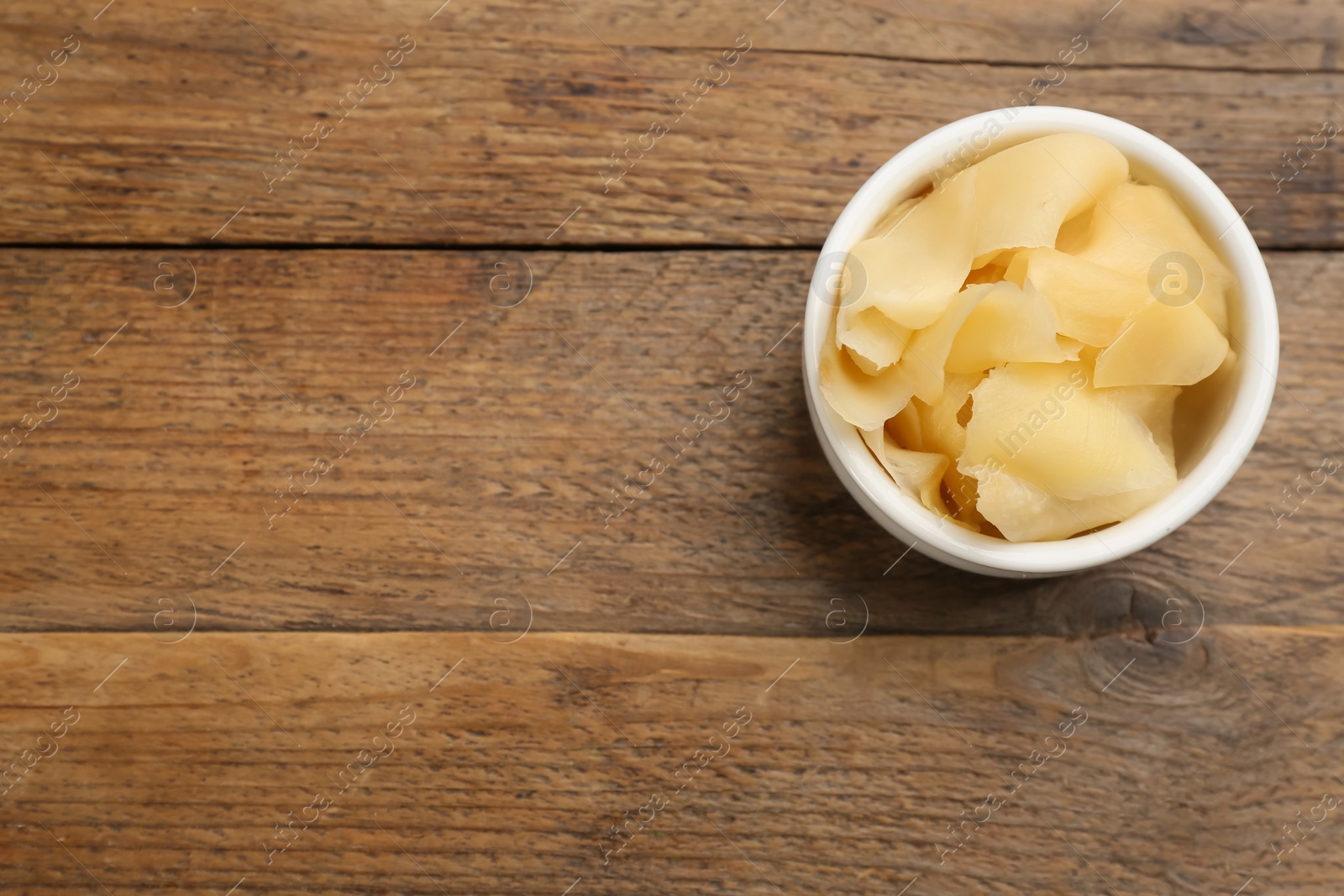 Photo of Pickled ginger in bowl on wooden table, top view. Space for text 