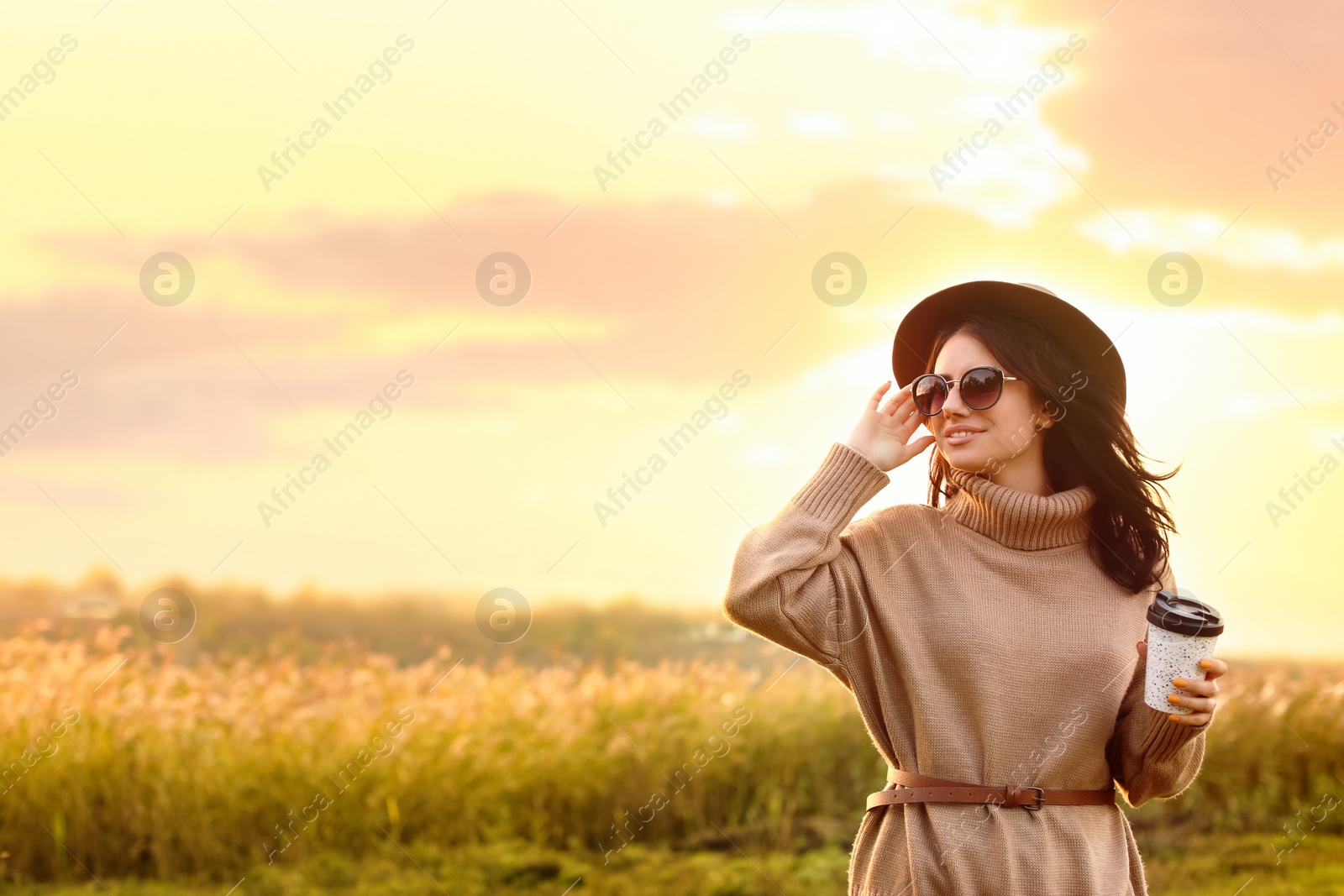 Photo of Beautiful young woman with cup of coffee wearing stylish autumn sweater outdoors