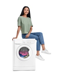 Beautiful woman sitting on washing machine with laundry against white background