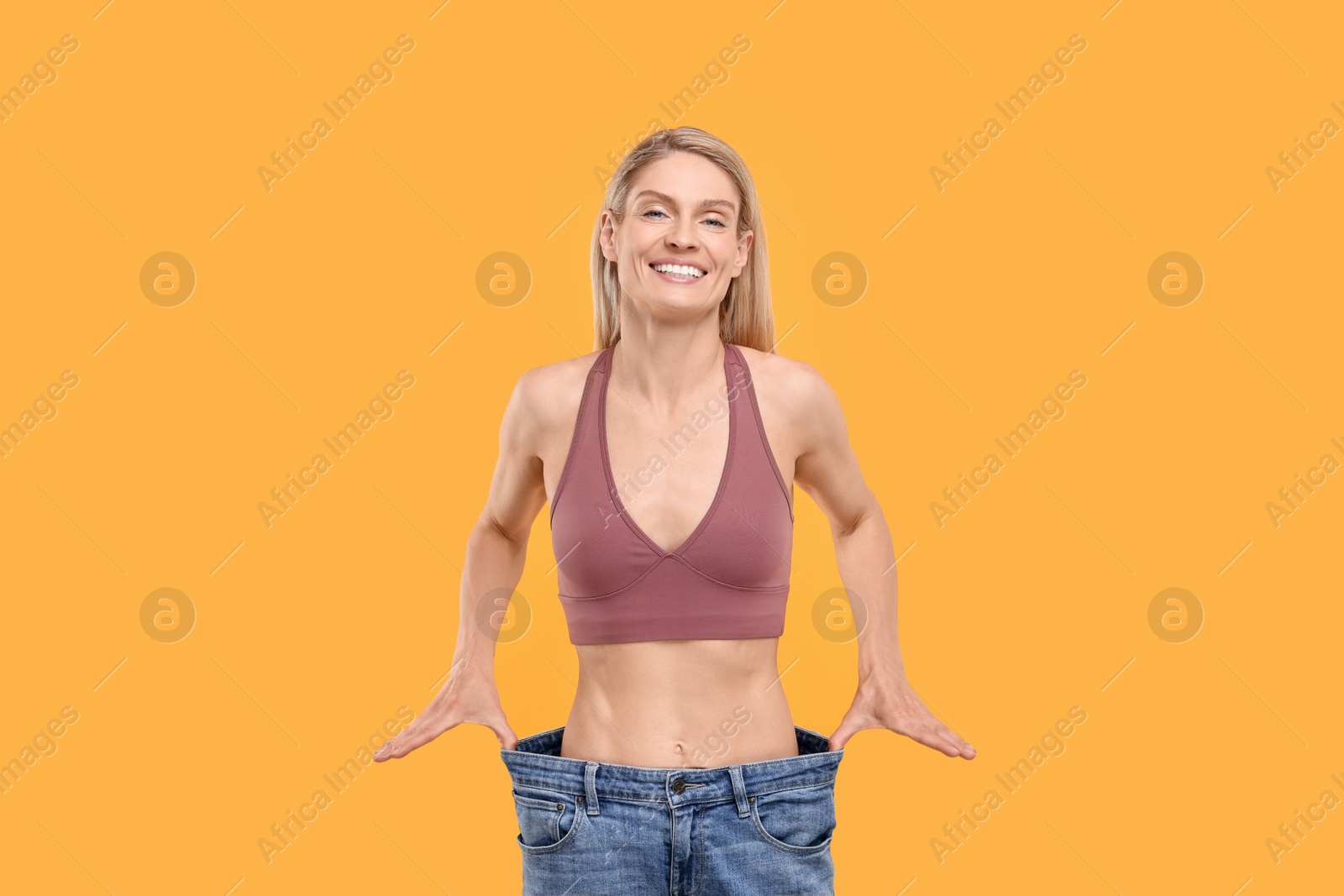Photo of Slim woman wearing big jeans on yellow background. Weight loss