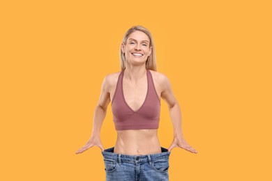 Photo of Slim woman wearing big jeans on yellow background. Weight loss