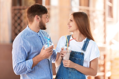 Photo of Young couple with cups of delicious milk shake outdoors