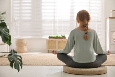 Photo of Woman meditating on wicker mat at home, back view. Space for text