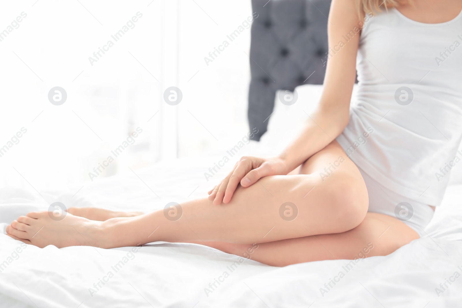 Photo of Young woman showing smooth silky skin after epilation on bed at home