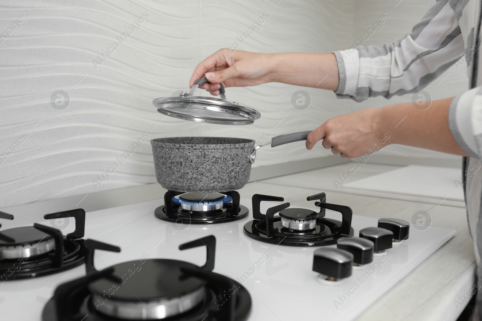 Photo of Woman putting pot on gas stove in kitchen, closeup