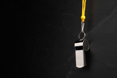 Photo of Referee equipment. Metal whistle on black textured background, closeup and space for text