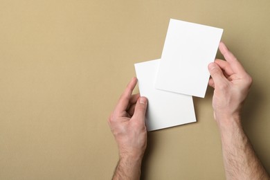 Man holding flyers on light brown background, top view. Mockup for design
