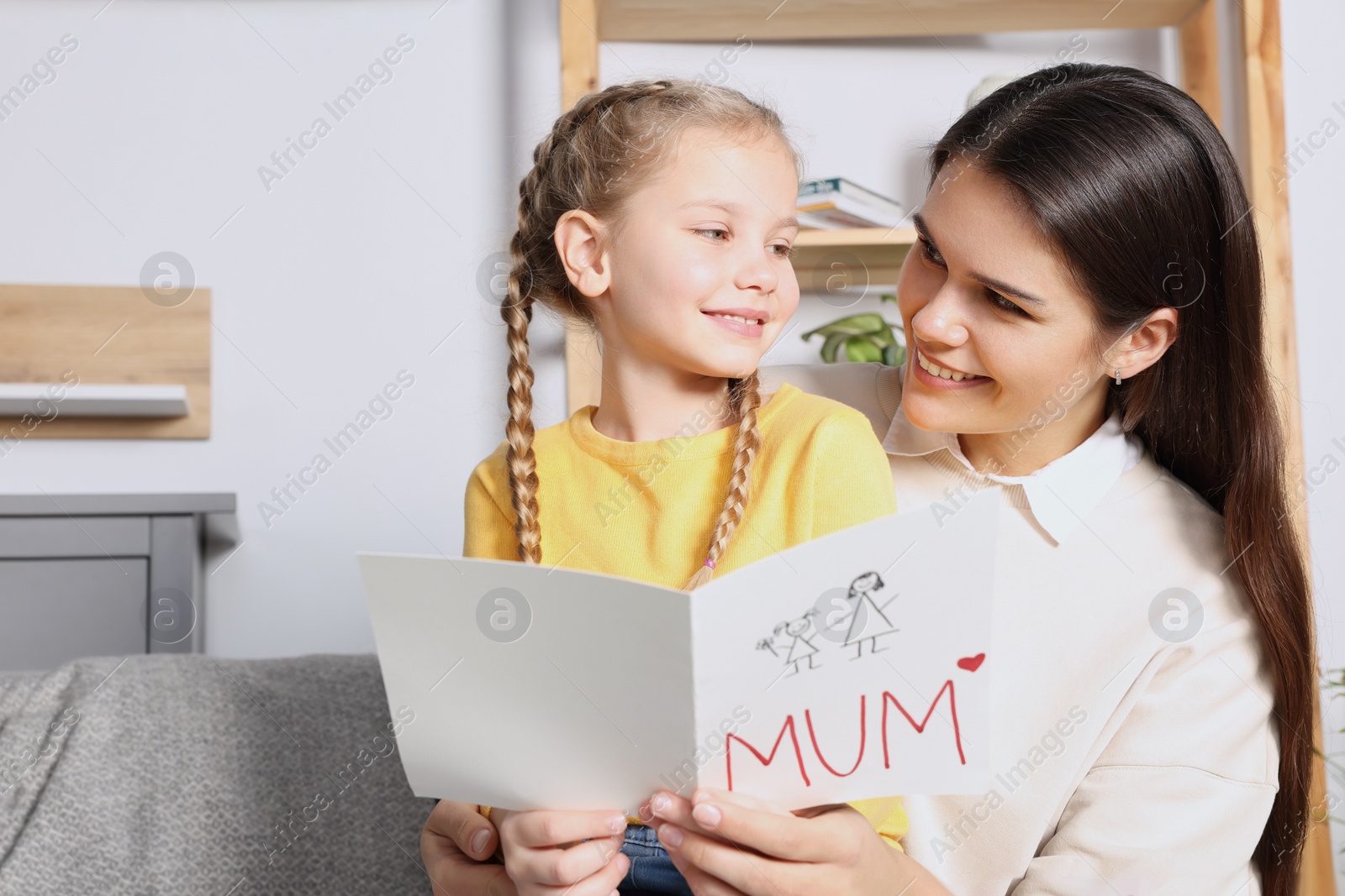 Photo of Happy woman receiving greeting card from her little daughter at home