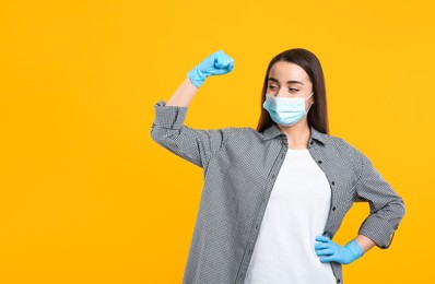 Photo of Woman with protective mask and gloves showing muscles on yellow background, space for text. Strong immunity concept