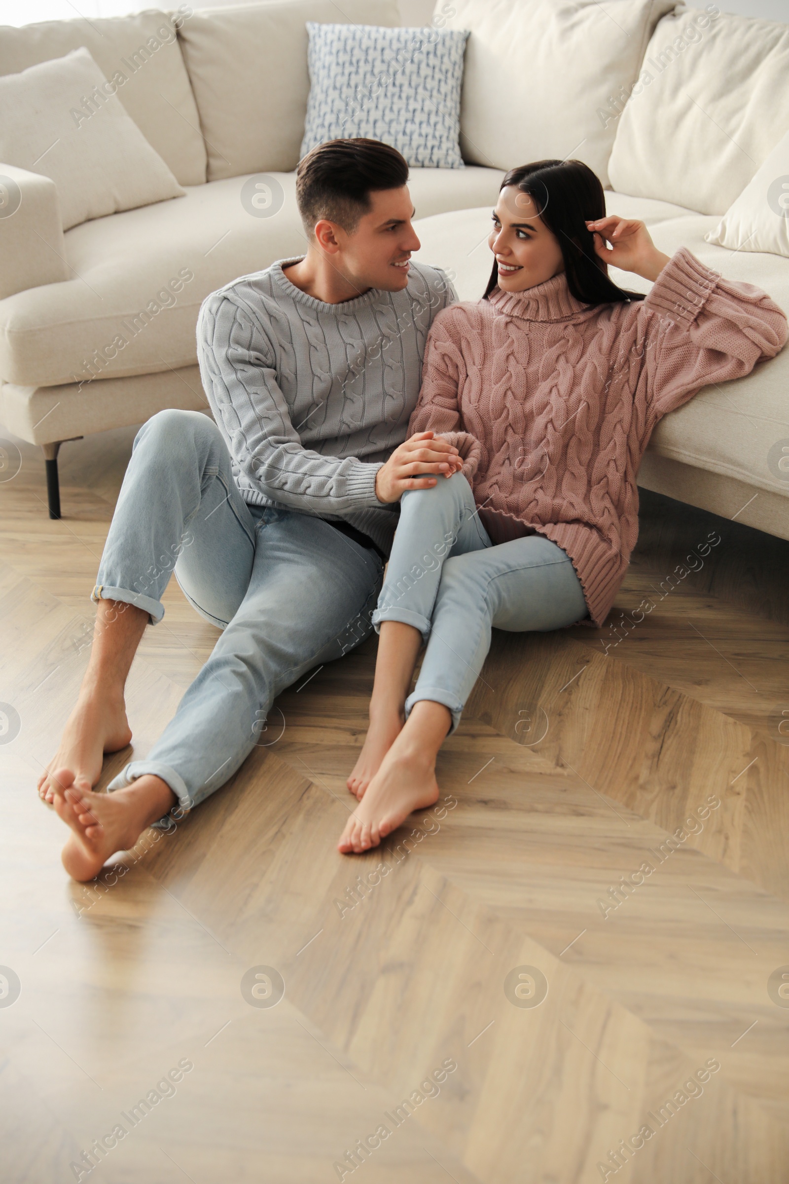 Photo of Happy couple sitting on warm floor in living room. Heating system