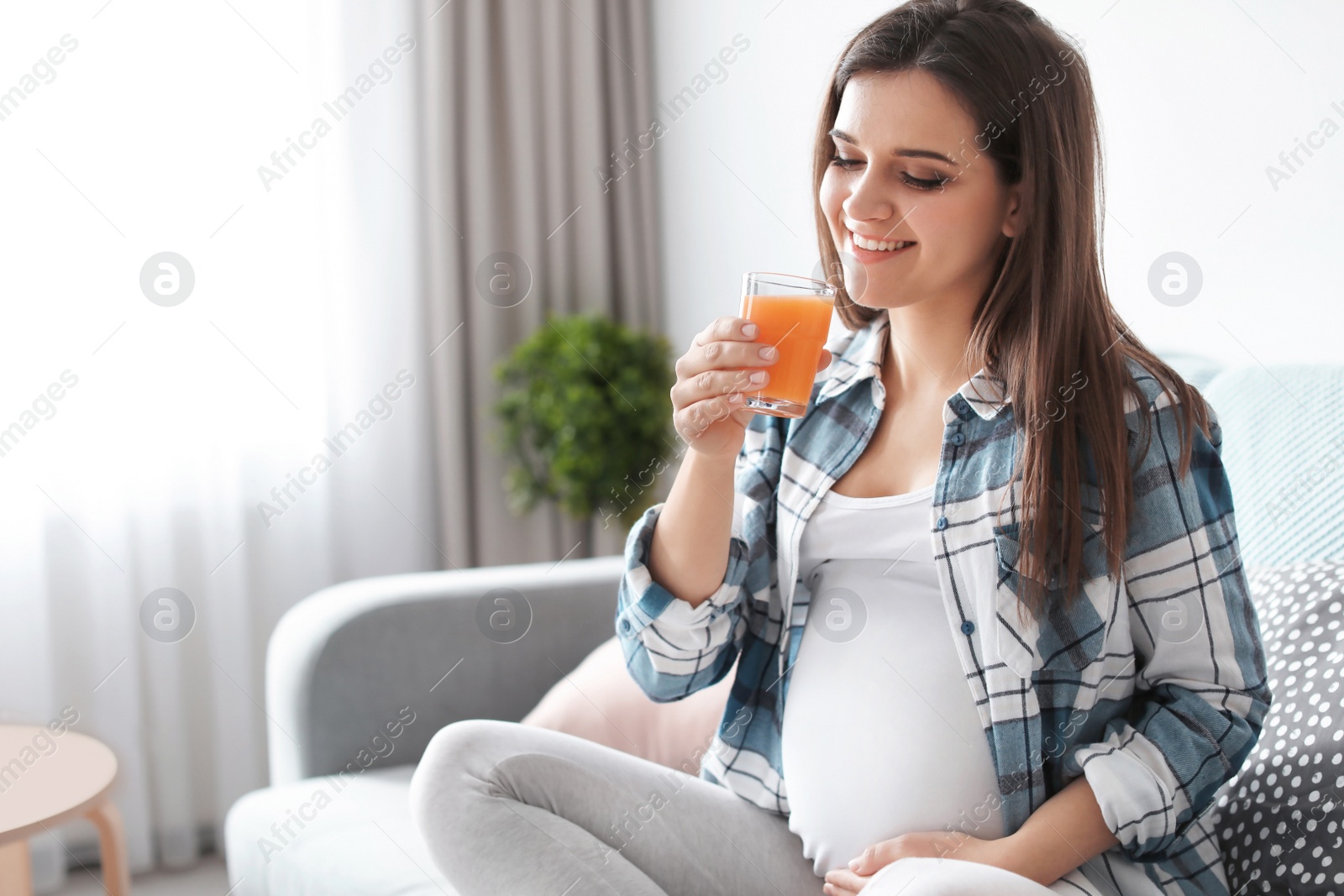 Photo of Young pregnant woman holding glass with juice at home