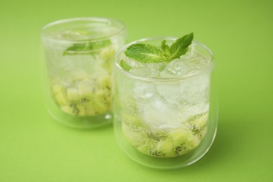 Photo of Glasses of refreshing drink with kiwi and mint on light green background, closeup