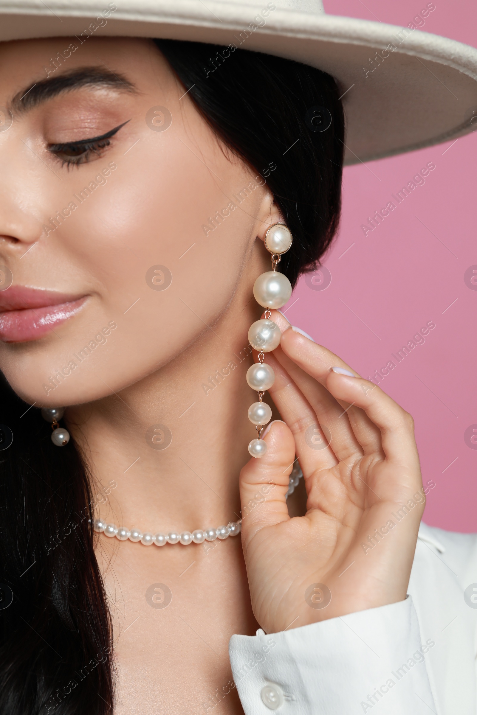 Photo of Young woman wearing elegant pearl jewelry on pink background, closeup