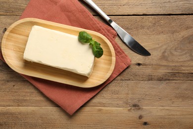 Photo of Block of tasty butter with basil and knife on wooden table, top view