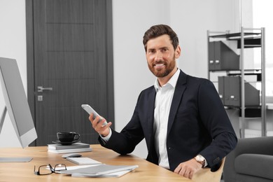 Smiling bearded man with smartphone at table in office