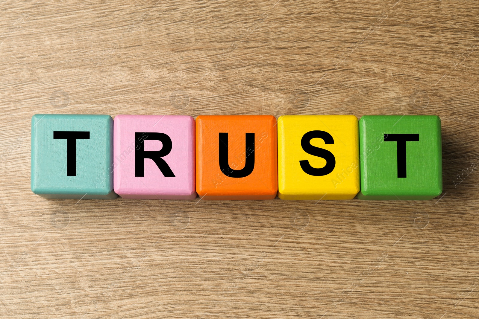 Photo of Colorful cubes with word TRUST on wooden table, flat lay