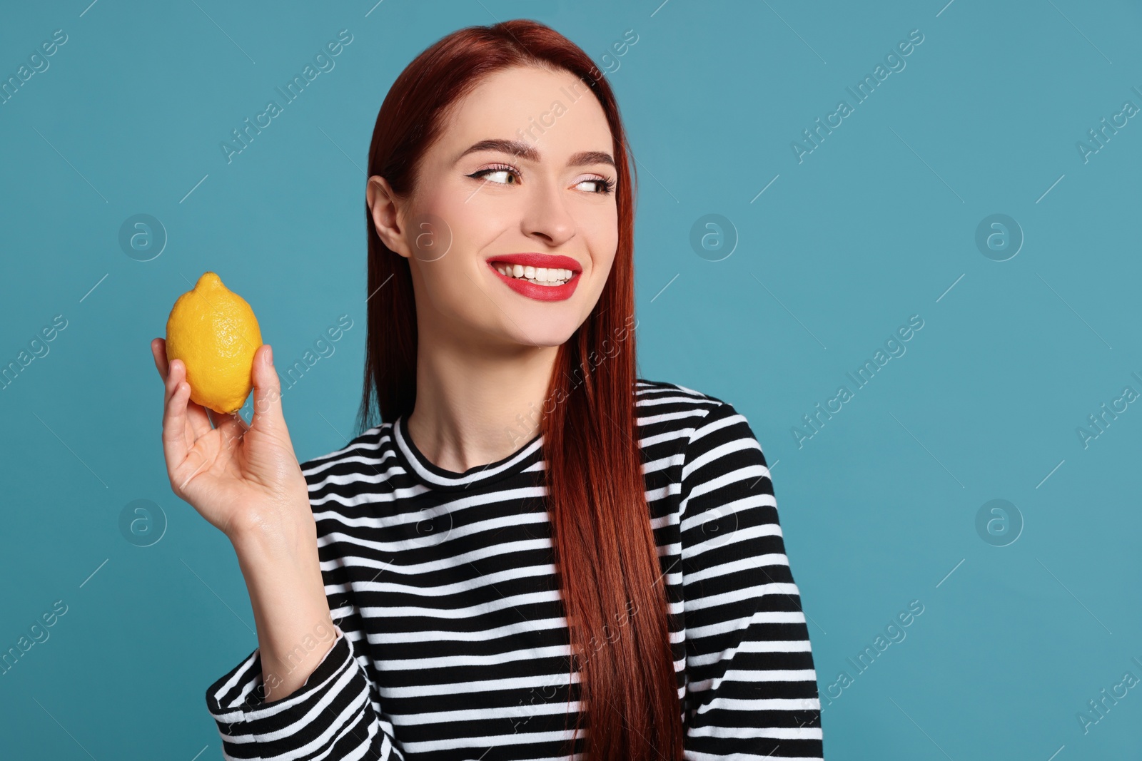 Photo of Happy woman with red dyed hair holding whole lemon on light blue background