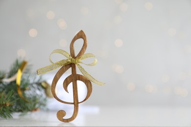Photo of Wooden music note with golden bow on light grey table against blurred Christmas lights. Space for text