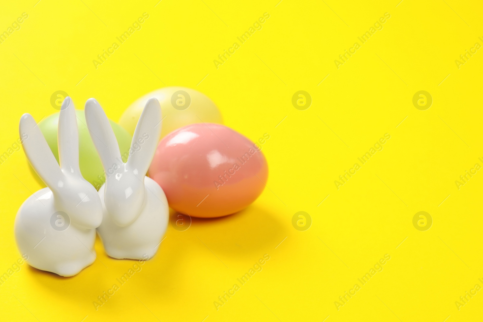 Photo of Ceramic Easter bunnies and dyed eggs on color background, space for text