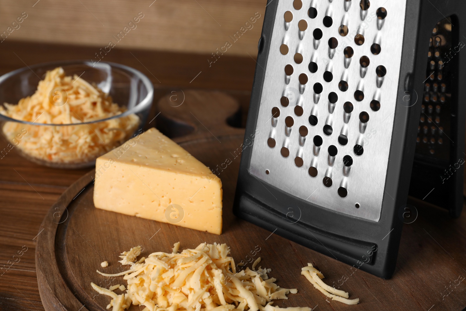 Photo of Grater and delicious cheese on wooden board, closeup