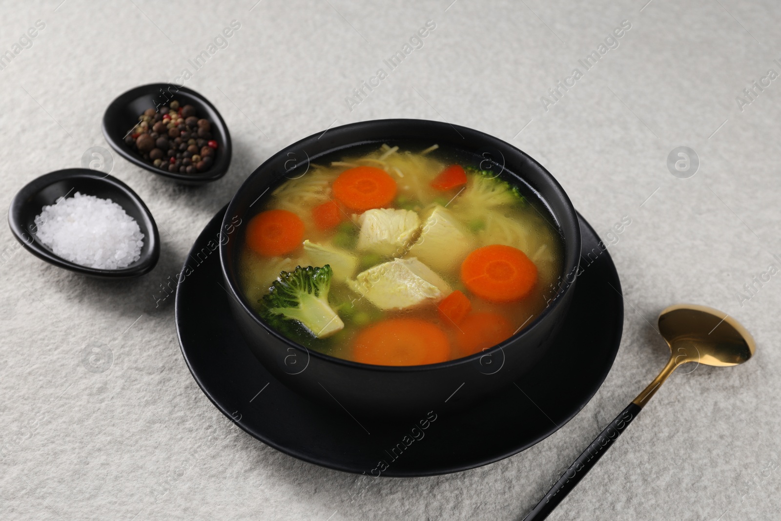 Photo of Tasty chicken soup with noodles and vegetables in bowl served on light textured table