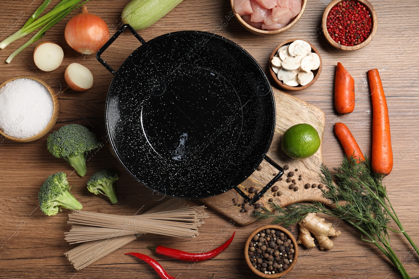 Photo of Empty iron wok surrounded by raw ingredients on wooden table, flat lay