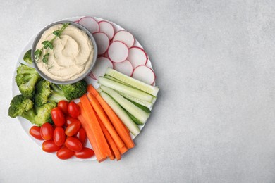 Photo of Plate with delicious hummus and fresh vegetables on light grey table, top view. Space for text