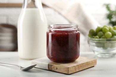 Jar of delicious gooseberry jam, fresh berries and milk on white table