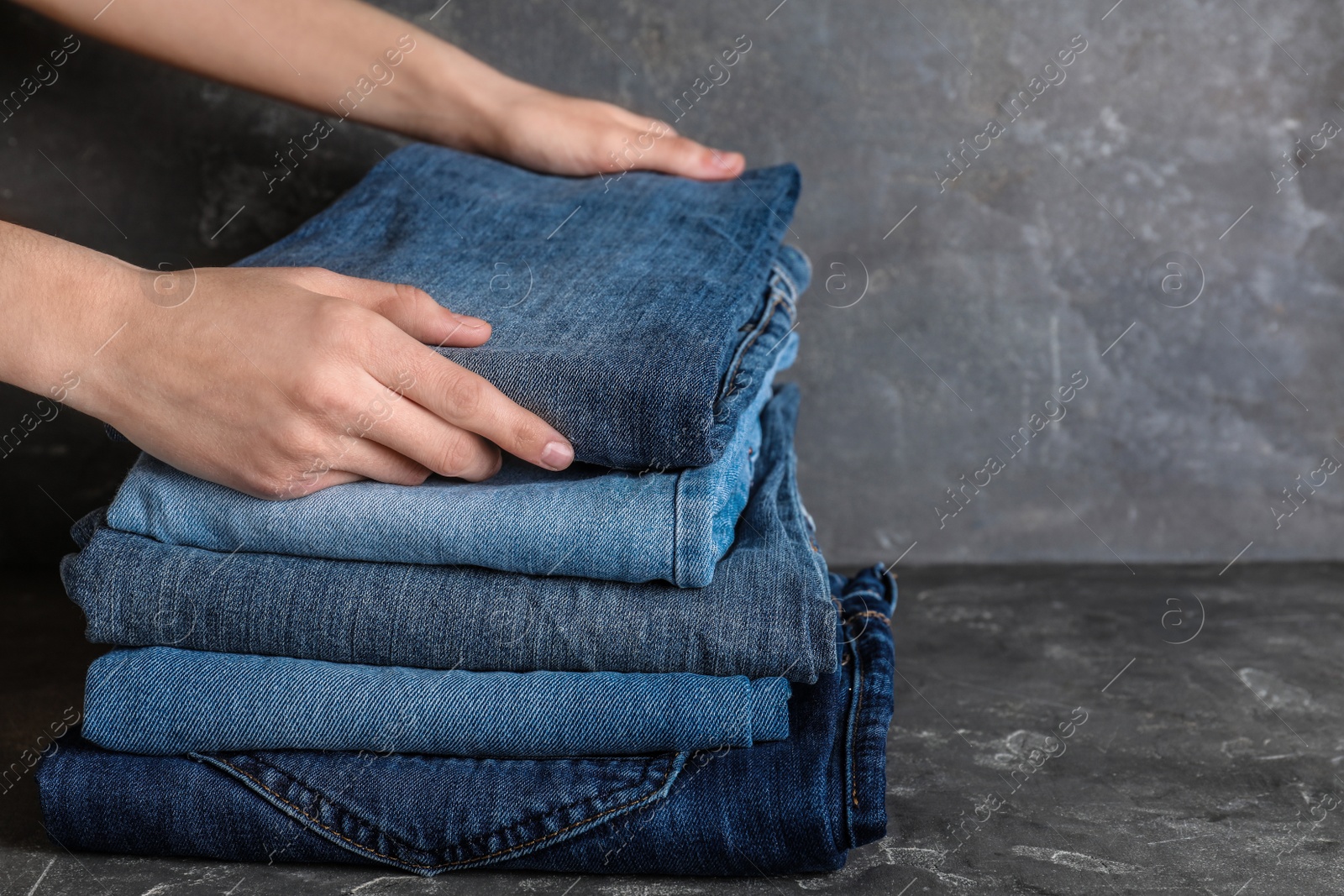 Photo of Woman folding stylish jeans on grey table, closeup. Space for text
