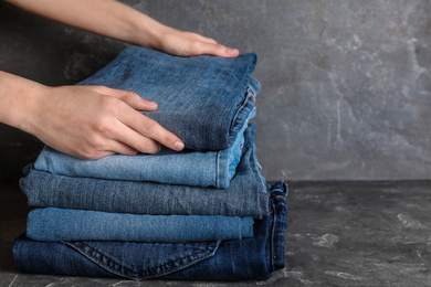 Woman folding stylish jeans on grey table, closeup. Space for text