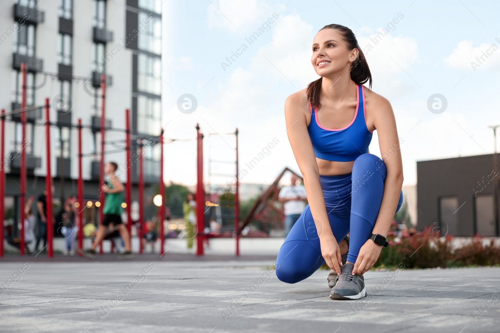 Photo of Beautiful woman in stylish sportswear tying shoelace near outdoor gym, space for text