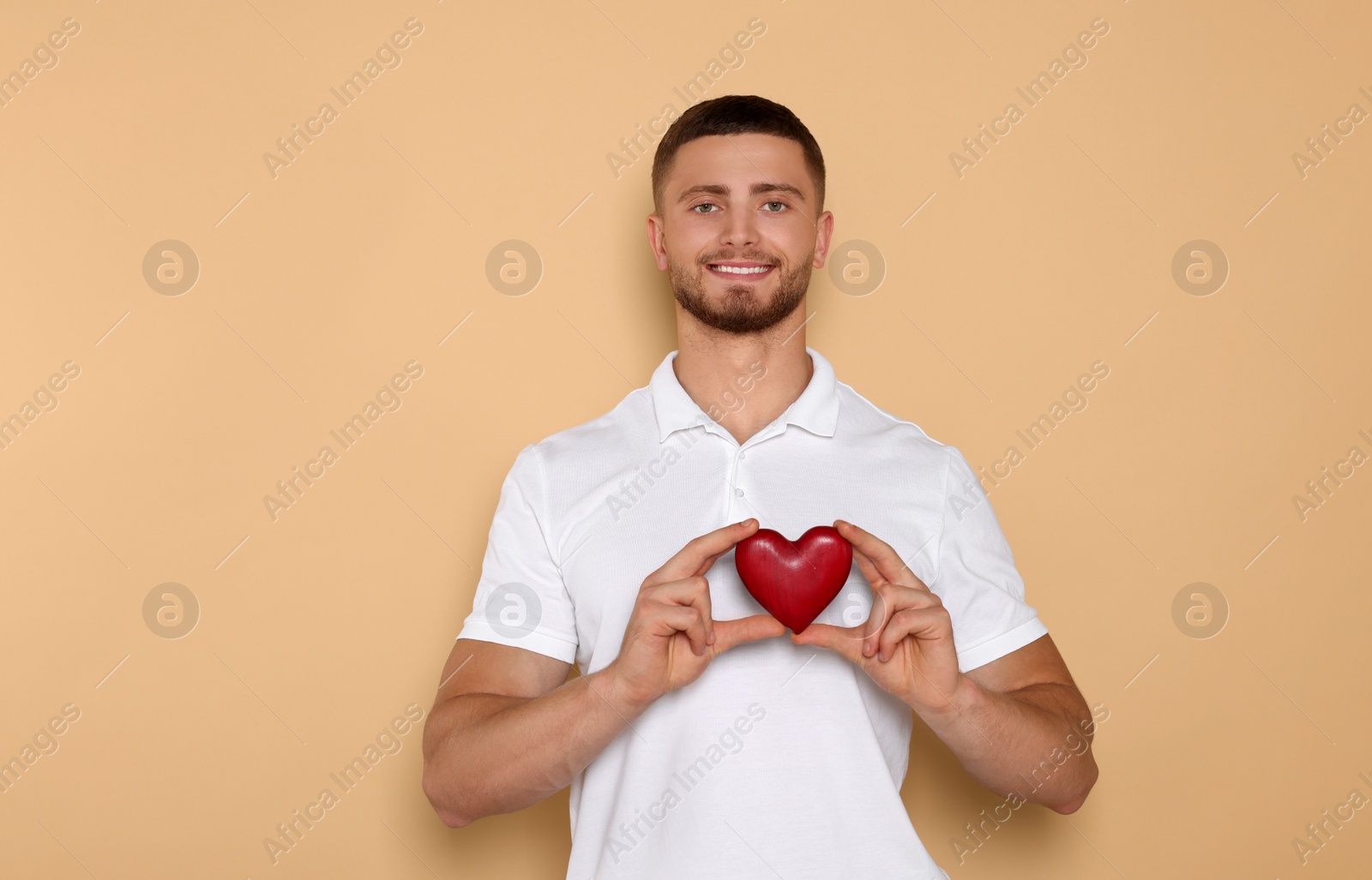 Photo of Happy volunteer holding red heart with hands on beige background