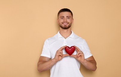 Photo of Happy volunteer holding red heart with hands on beige background