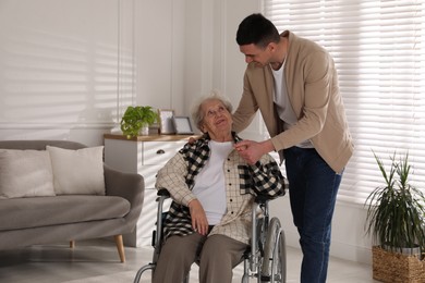 Photo of Young caregiver assisting senior woman in wheelchair indoors. Home care service