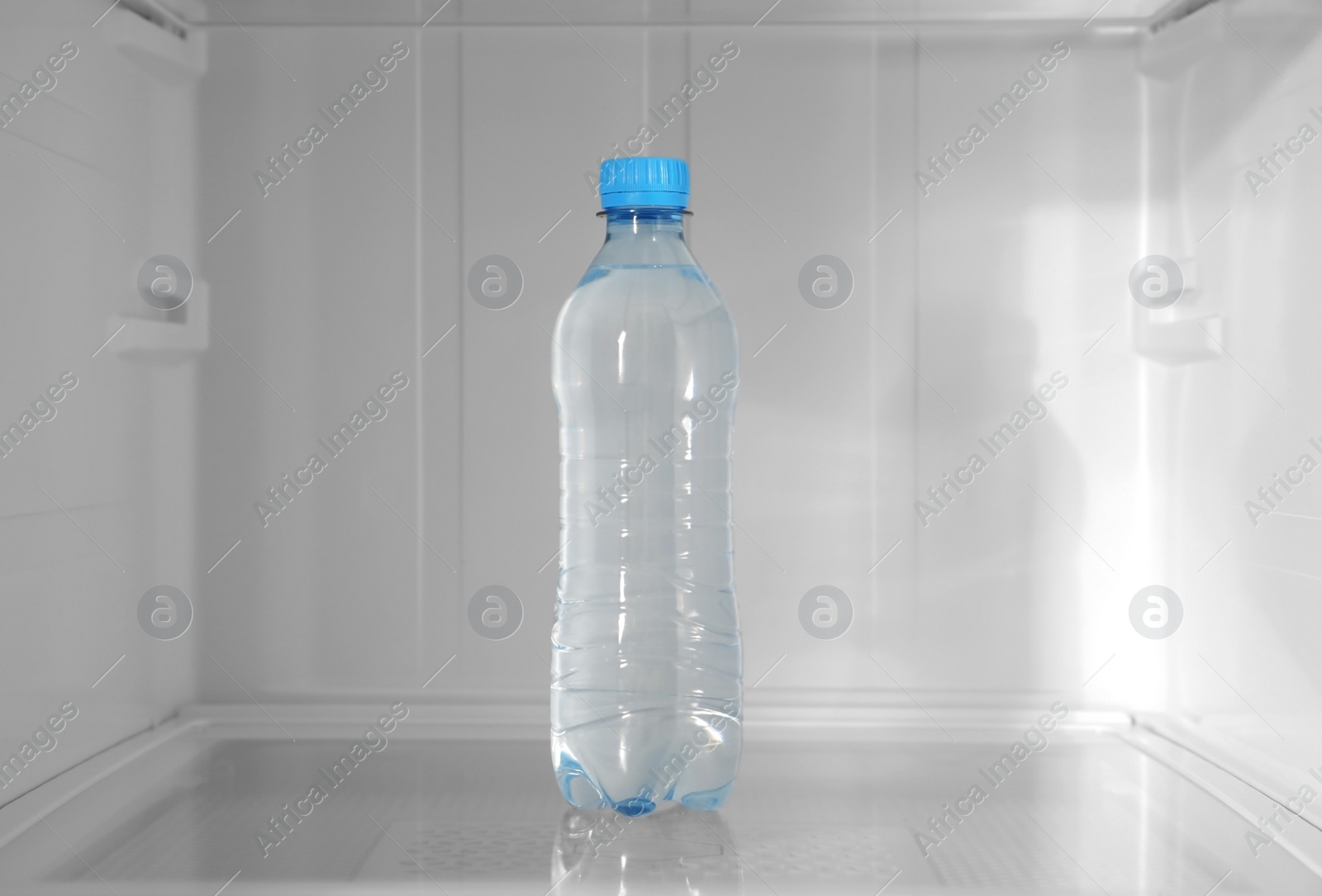 Photo of Bottle of water on shelf inside modern refrigerator