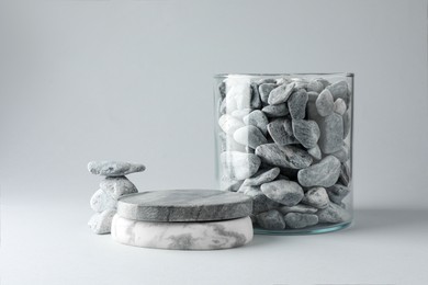 Photo of Presentation for product. Podium and glass container with stones on light grey background. Space for text