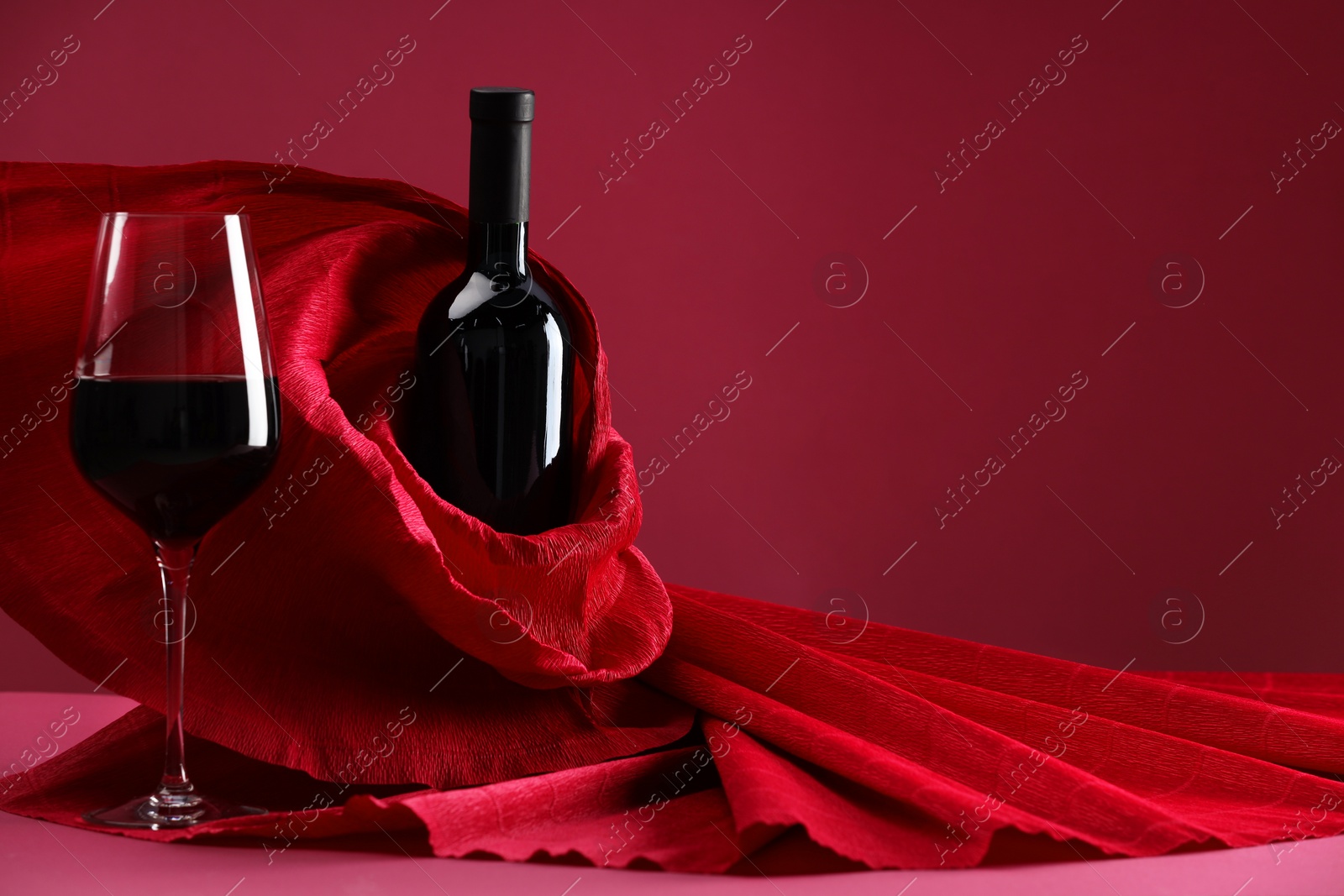 Photo of Stylish presentation of delicious red wine in bottle and glass on pink background. Space for text