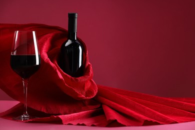 Photo of Stylish presentation of delicious red wine in bottle and glass on pink background. Space for text