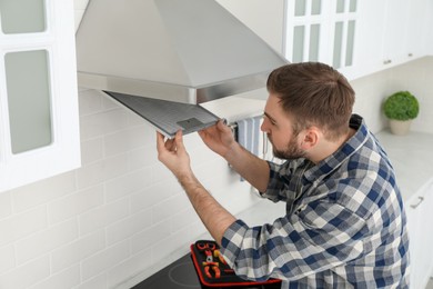 Man repairing modern cooker hood in kitchen