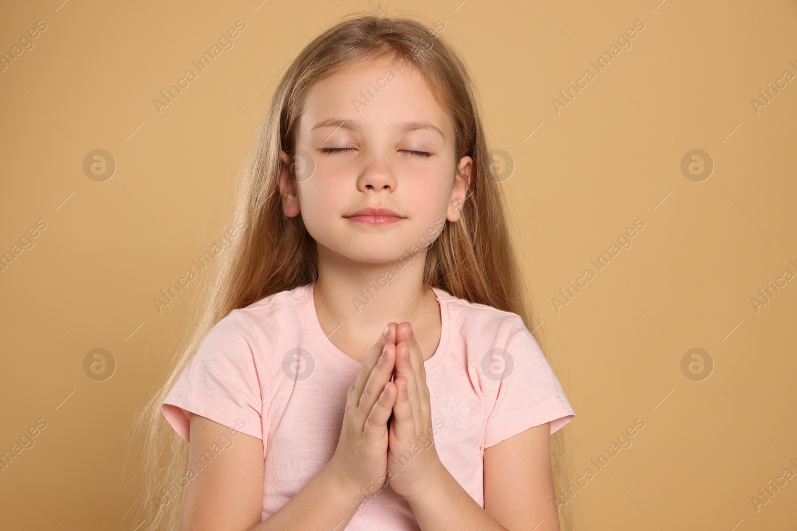 Photo of Girl with clasped hands praying on beige background